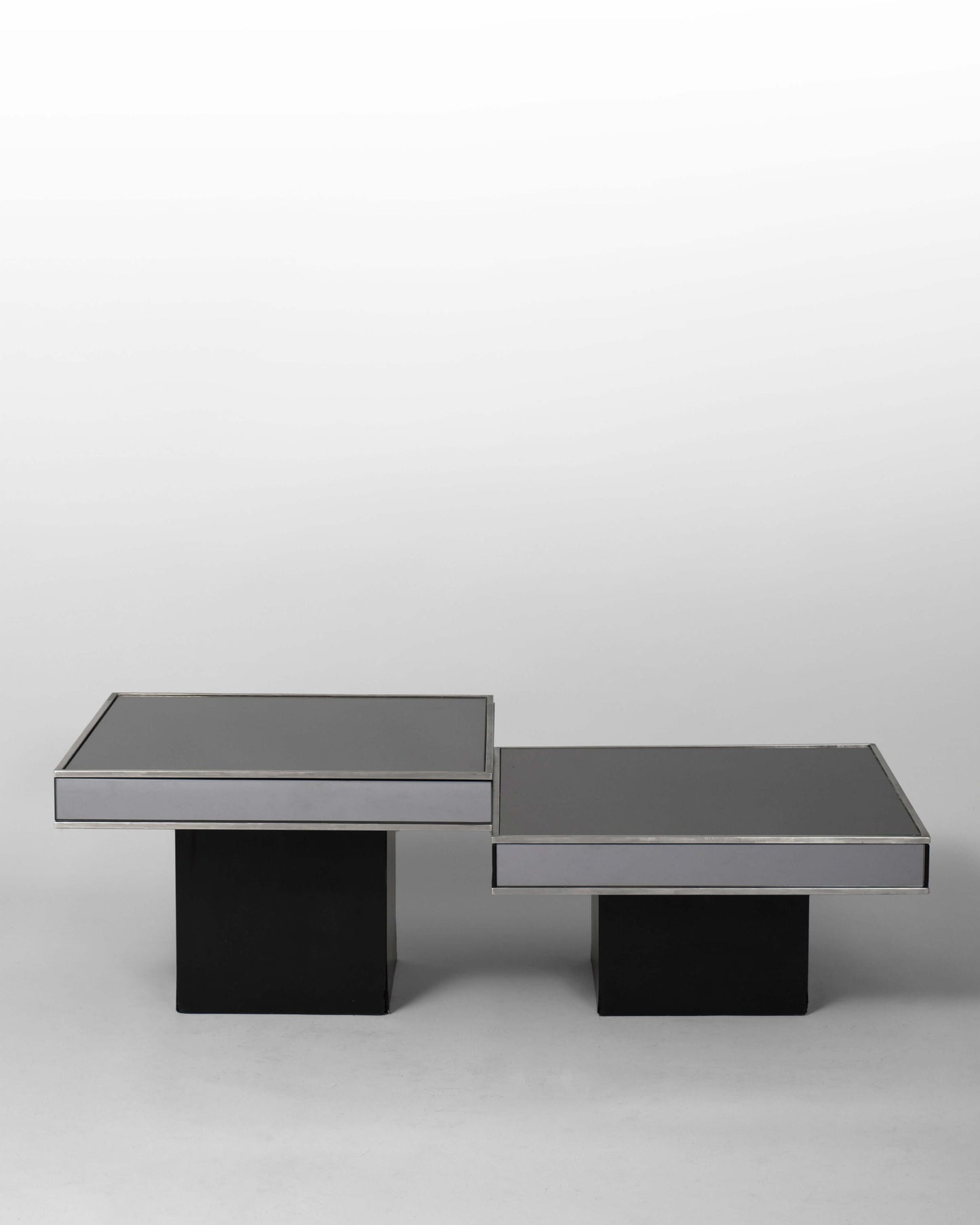 Pair of nesting tables designed by Willy Rizzo for Cidue in the 1970s, featuring chromed metal frames and black mirrored glass surfaces, blending Italian modernism with sculptural elegance.