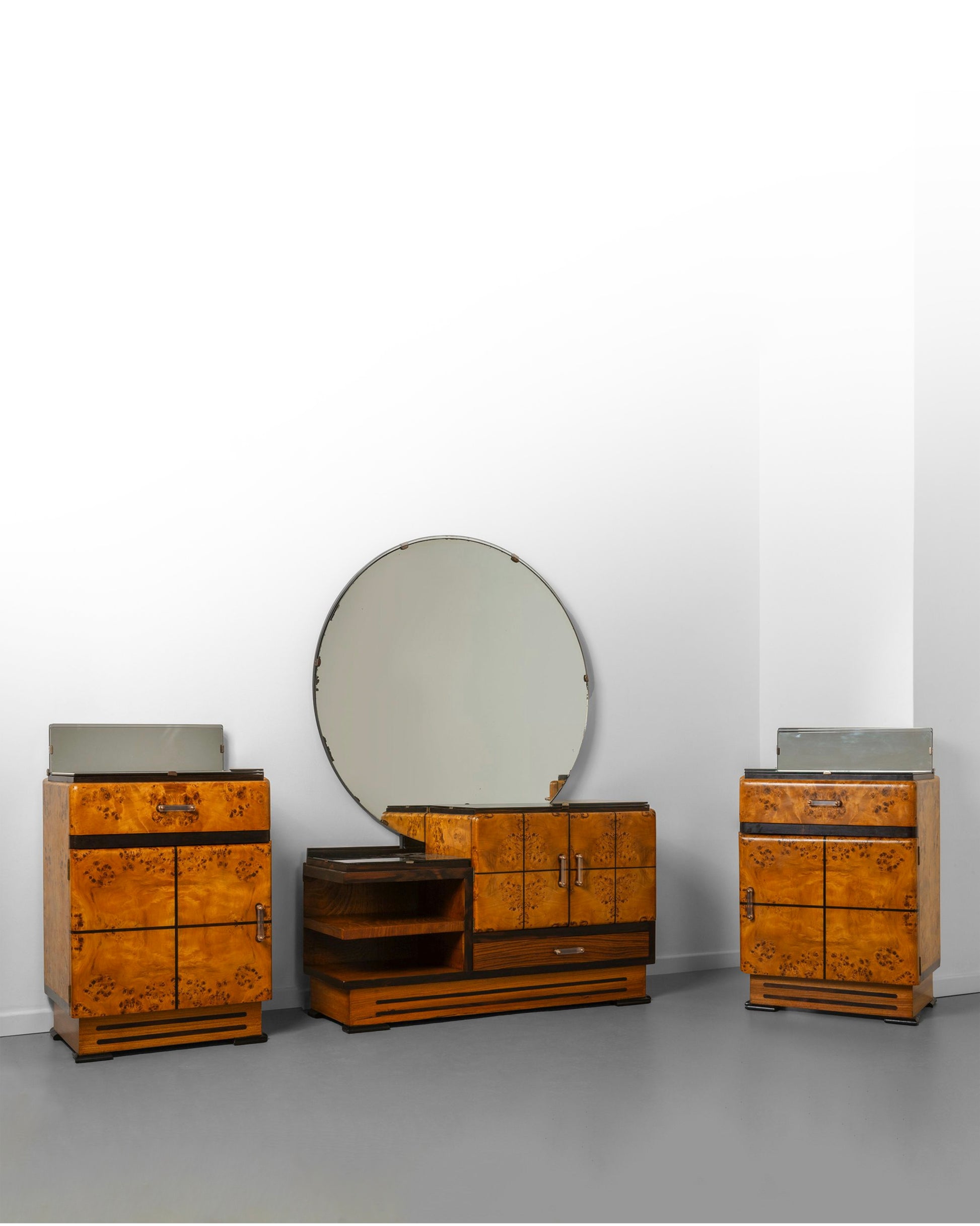 Art Deco bedroom set from the 1940s, crafted from elm wood with warm tones, including a dressing table with a round mirror and two matching nightstands, showcasing bold geometric lines and fine craftsmanship.