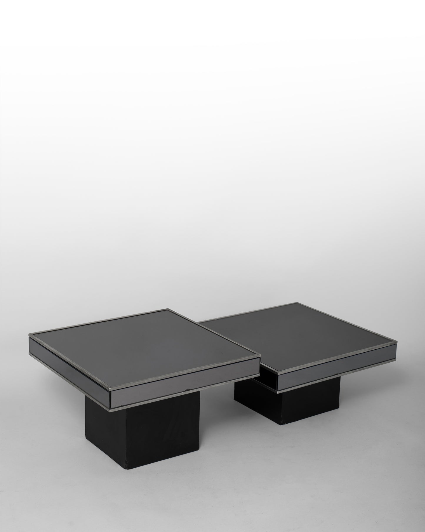 Pair of nesting tables designed by Willy Rizzo for Cidue in the 1970s, featuring chromed metal frames and black mirrored glass surfaces, blending Italian modernism with sculptural elegance.