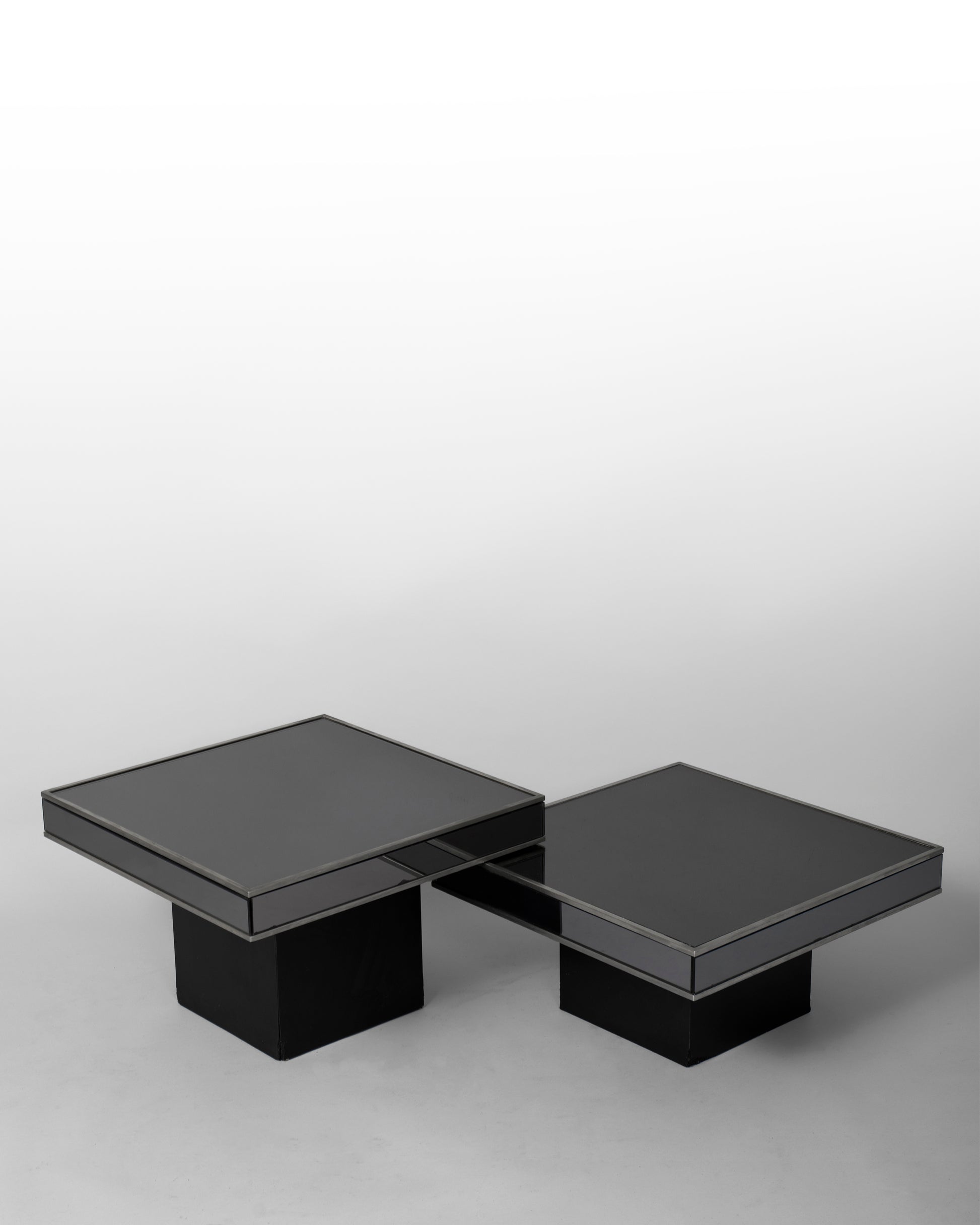 Pair of nesting tables designed by Willy Rizzo for Cidue in the 1970s, featuring chromed metal frames and black mirrored glass surfaces, blending Italian modernism with sculptural elegance.