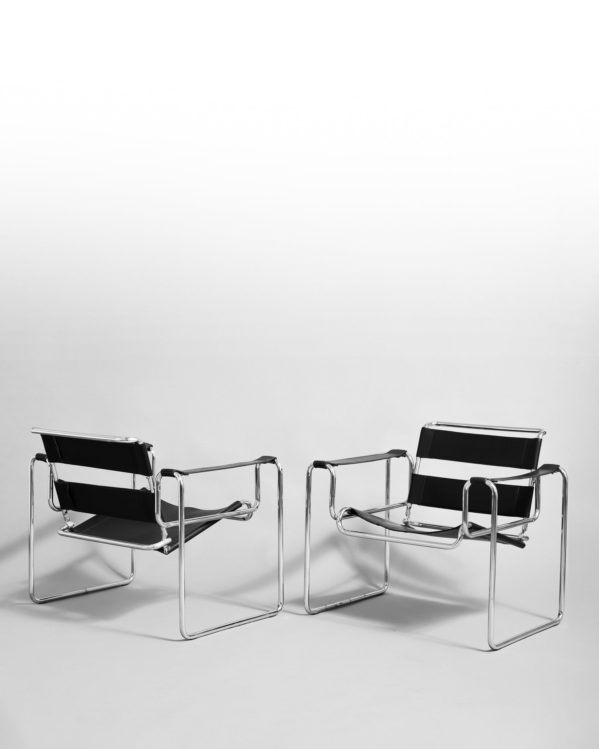 Pair of modernist armchairs inspired by the Wassily chair by Marcel Breuer, reissued in the 1990s, featuring black leather seats and chrome steel tubing, epitomizing Bauhaus minimalism and avant-garde design.