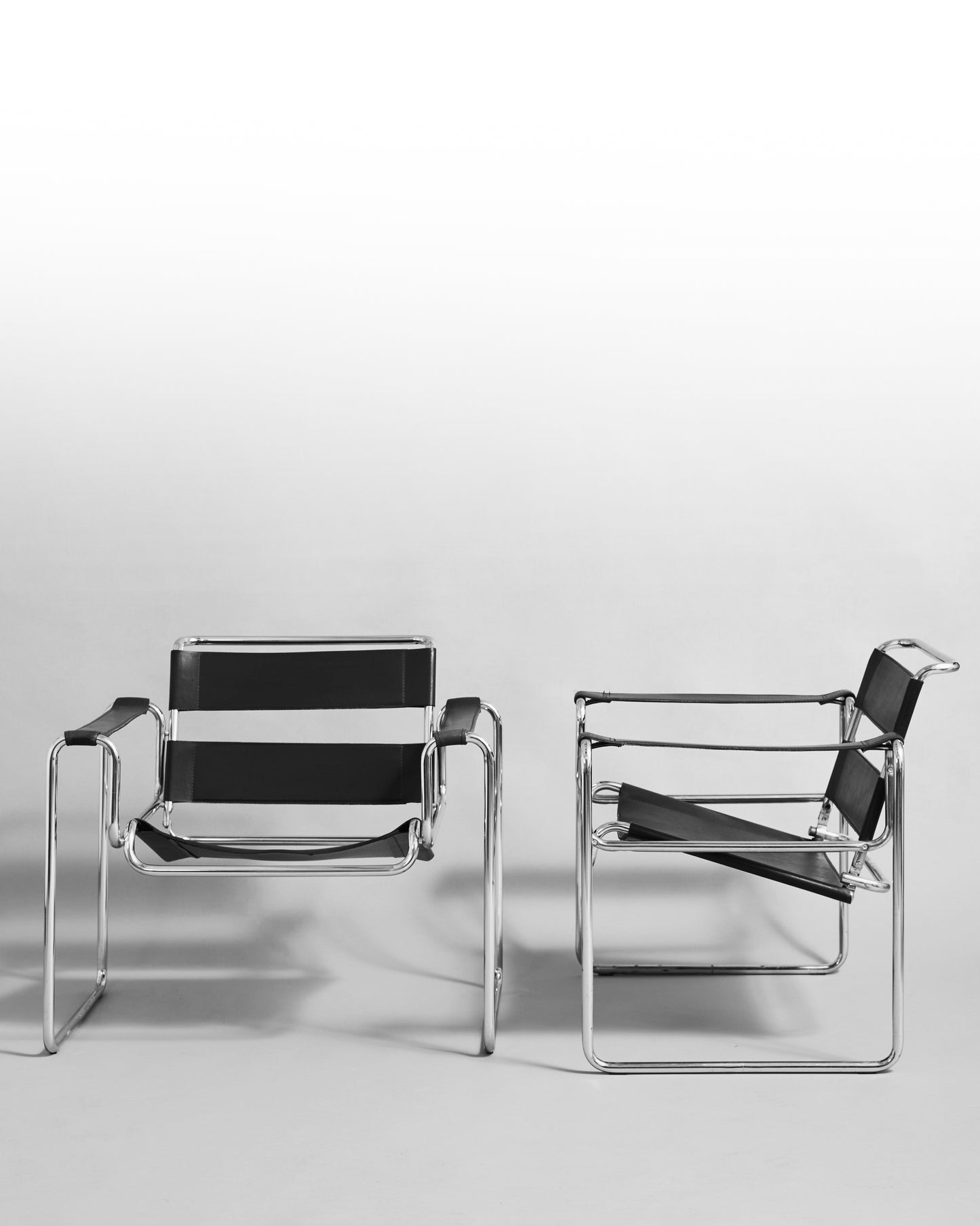 Pair of modernist armchairs inspired by the Wassily chair by Marcel Breuer, reissued in the 1990s, featuring black leather seats and chrome steel tubing, epitomizing Bauhaus minimalism and avant-garde design.