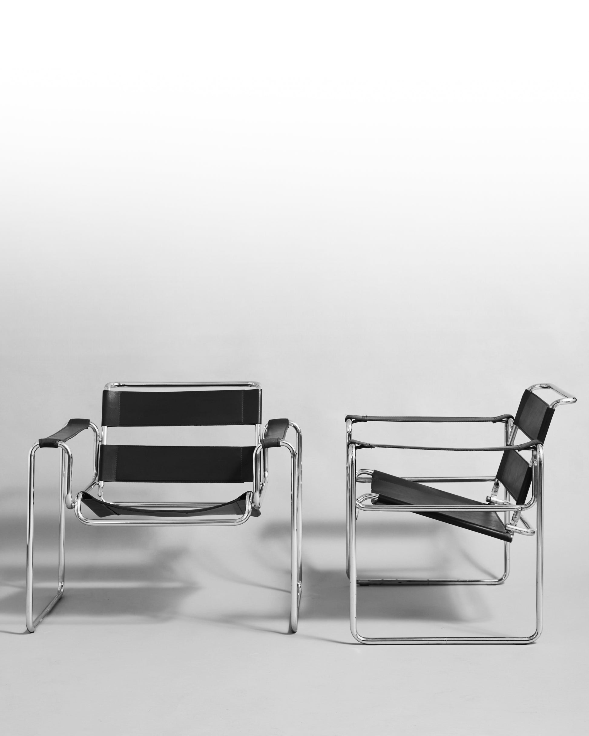 Pair of modernist armchairs inspired by the Wassily chair by Marcel Breuer, reissued in the 1990s, featuring black leather seats and chrome steel tubing, epitomizing Bauhaus minimalism and avant-garde design.