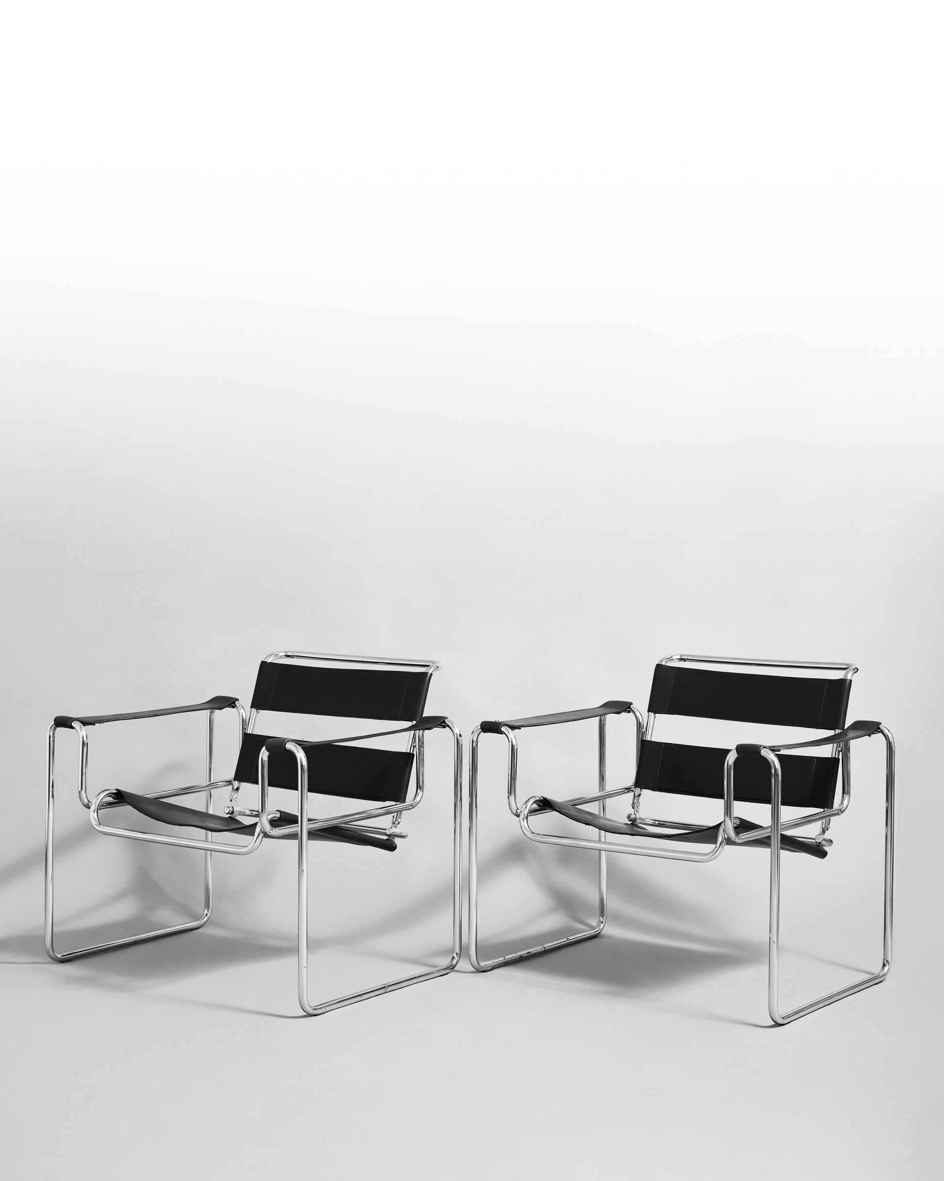 Pair of modernist armchairs inspired by the Wassily chair by Marcel Breuer, reissued in the 1990s, featuring black leather seats and chrome steel tubing, epitomizing Bauhaus minimalism and avant-garde design.