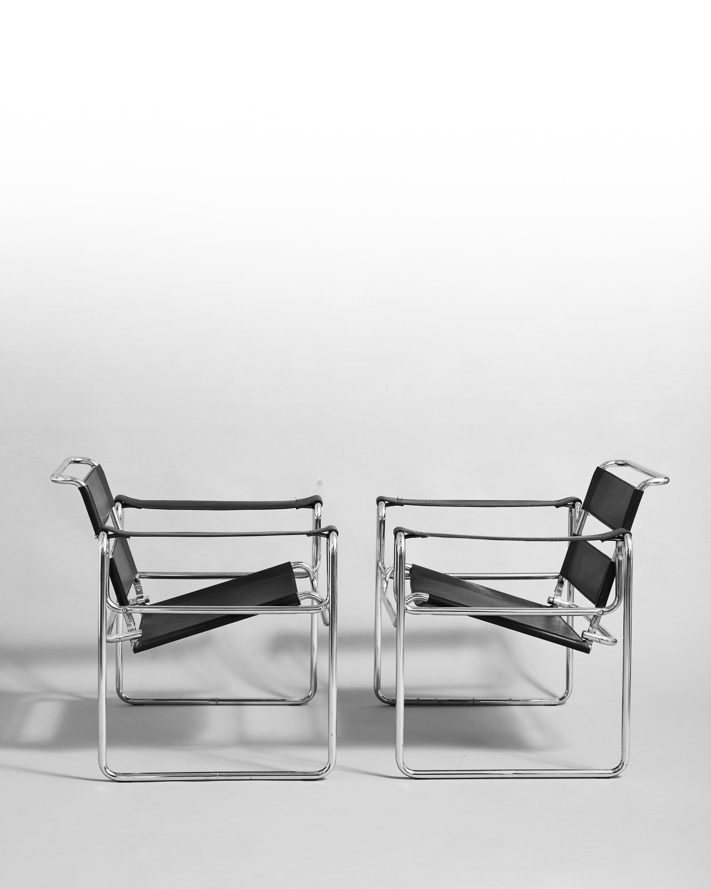 Pair of modernist armchairs inspired by the Wassily chair by Marcel Breuer, reissued in the 1990s, featuring black leather seats and chrome steel tubing, epitomizing Bauhaus minimalism and avant-garde design.