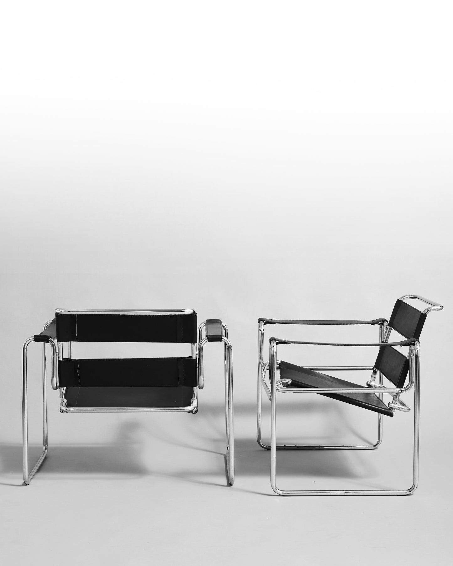 Pair of modernist armchairs inspired by the Wassily chair by Marcel Breuer, reissued in the 1990s, featuring black leather seats and chrome steel tubing, epitomizing Bauhaus minimalism and avant-garde design.