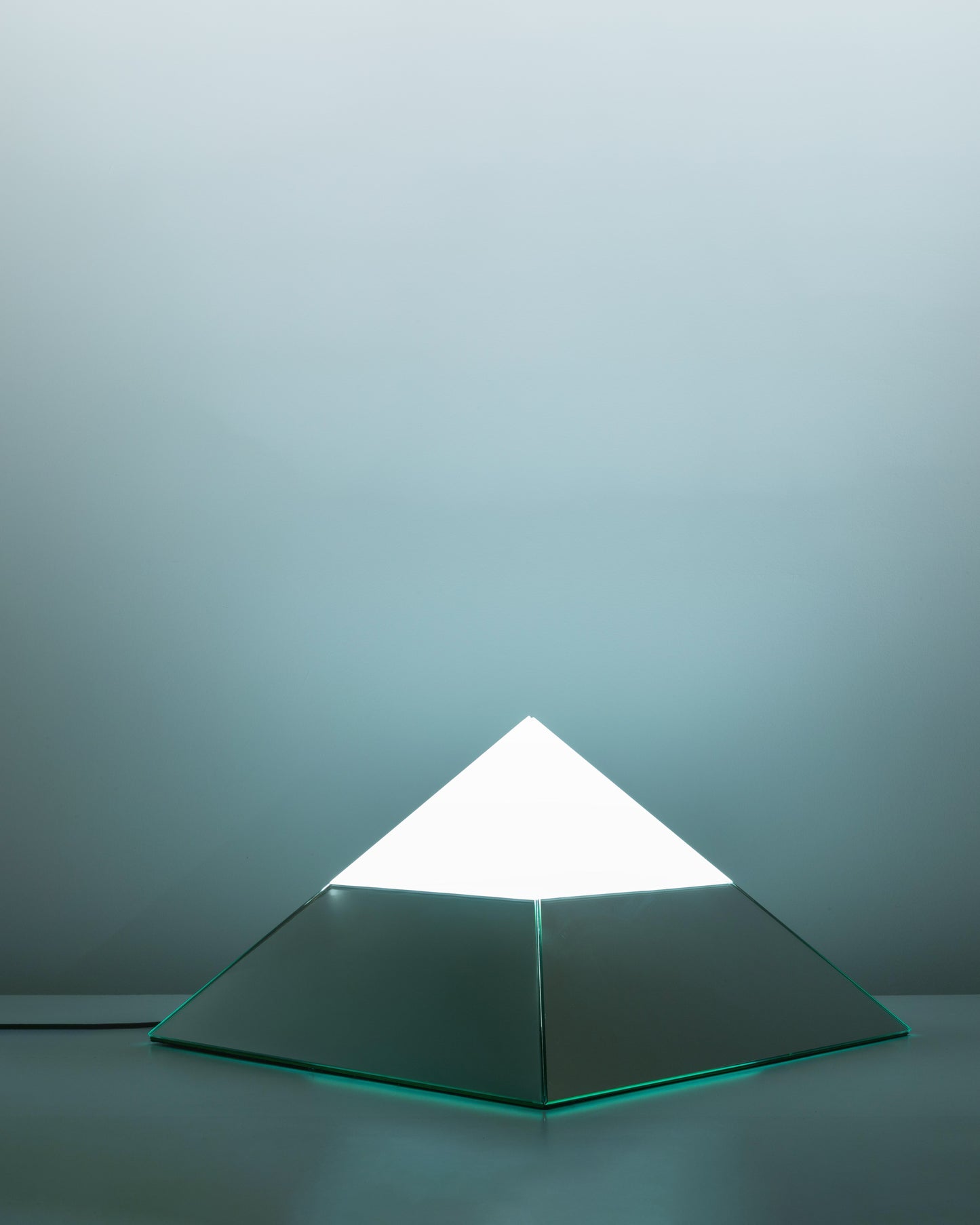 Pyramidal lamp from Italy, crafted in the 1970s with reflective glass surfaces and a striking geometric design, emitting a soft glow and blending modernist aesthetics with architectural elegance.