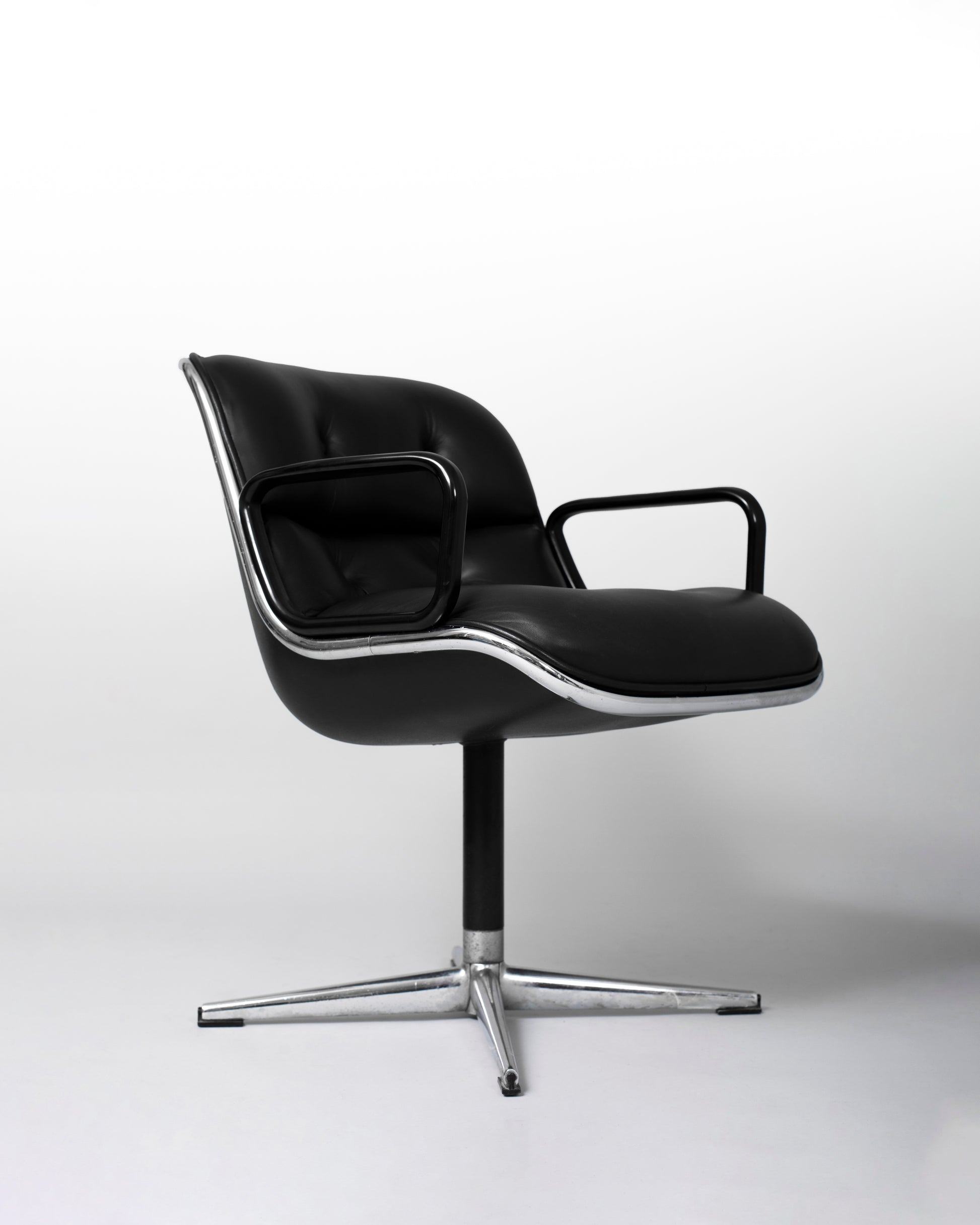 Stationary armchair designed by Charles Pollock for Knoll International in the 1960s, featuring a black leather seat, chrome star-shaped base, and mid-century modern design with geometric elegance.