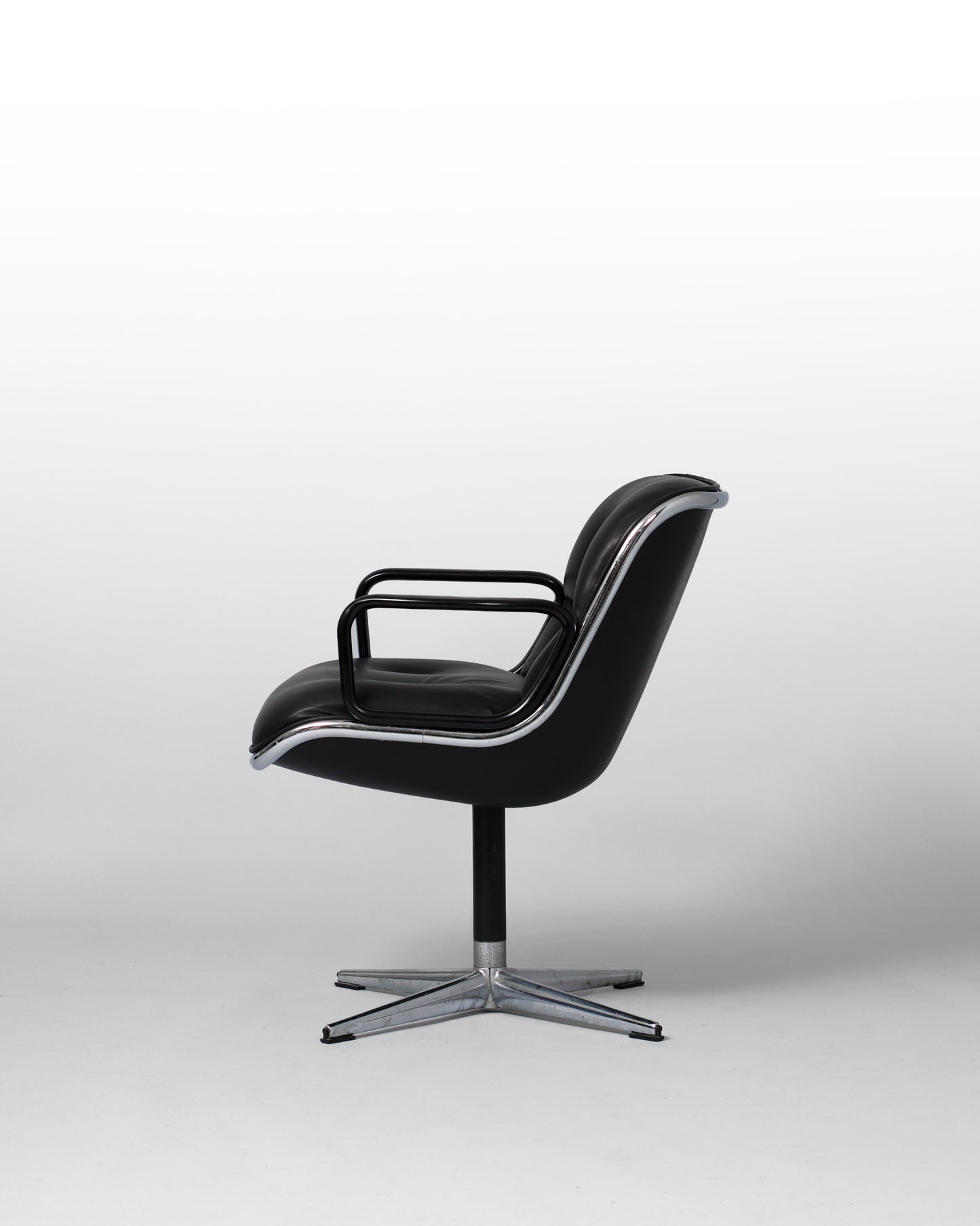 Stationary armchair designed by Charles Pollock for Knoll International in the 1960s, featuring a black leather seat, chrome star-shaped base, and mid-century modern design with geometric elegance.