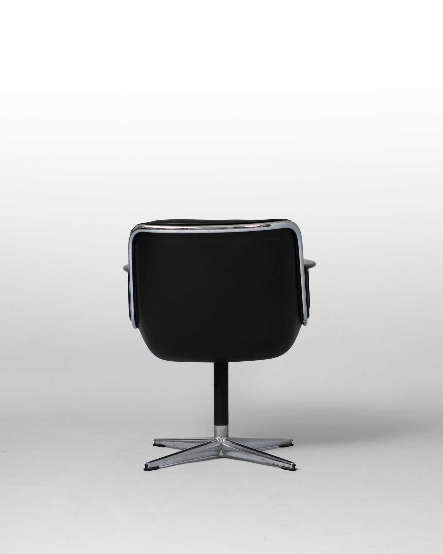 Stationary armchair designed by Charles Pollock for Knoll International in the 1960s, featuring a black leather seat, chrome star-shaped base, and mid-century modern design with geometric elegance.