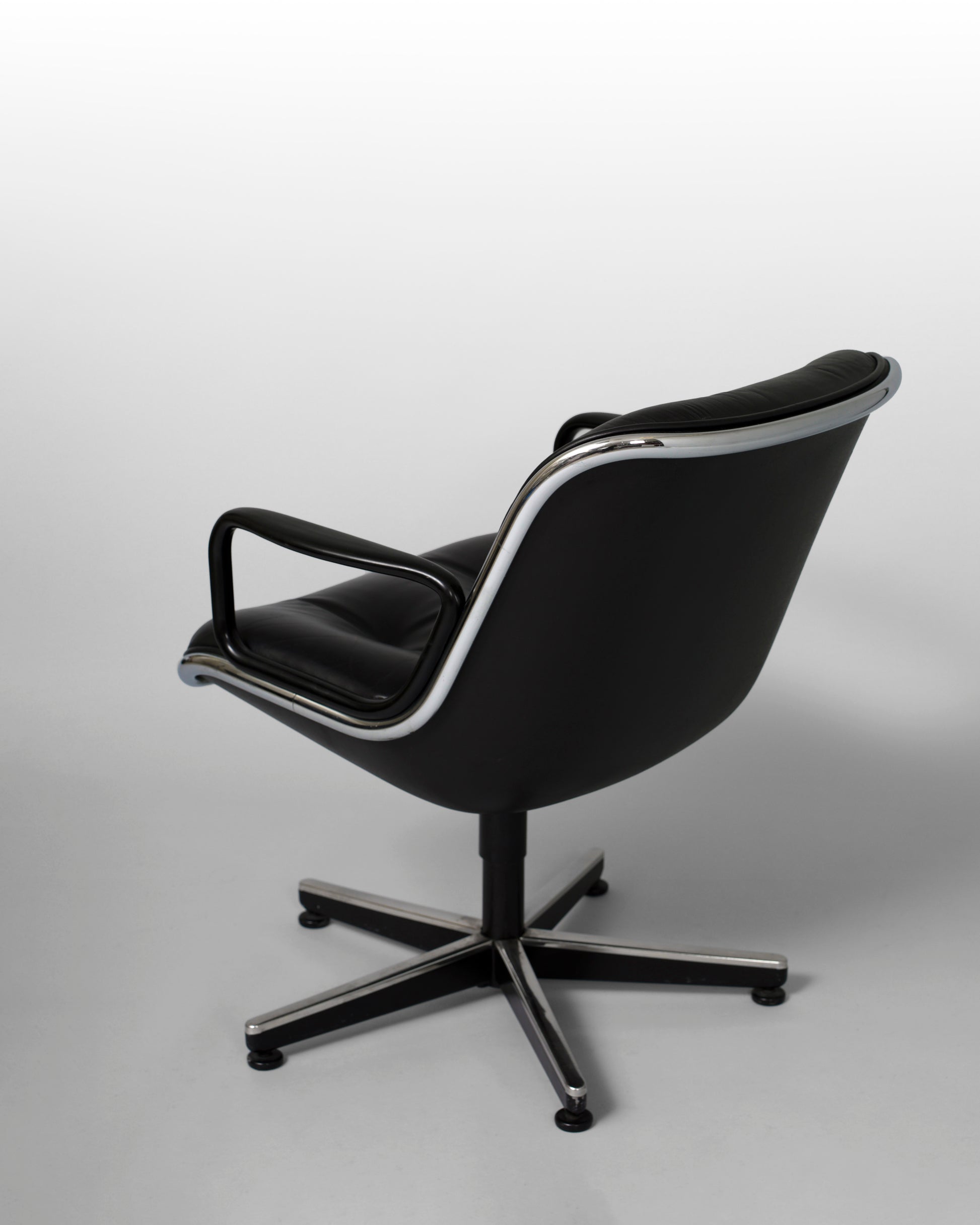 Swivel armchair designed by Charles Pollock for Knoll International in the 1960s, featuring a black leather seat, chrome star-shaped rotating base, and mid-century modern aesthetics, combining comfort with geometric elegance.