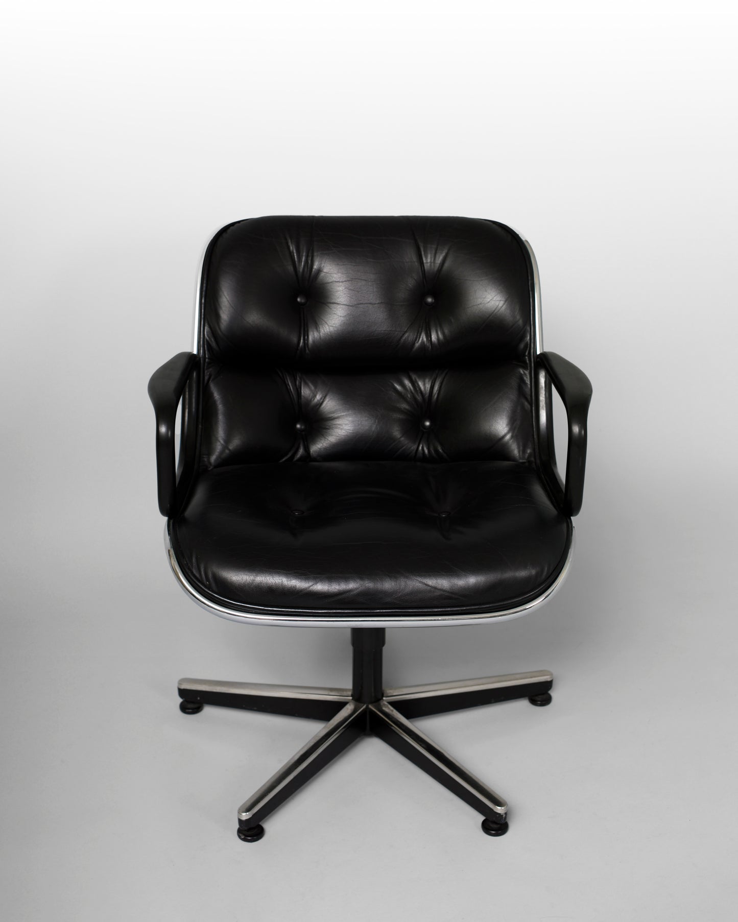 Swivel armchair designed by Charles Pollock for Knoll International in the 1960s, featuring a black leather seat, chrome star-shaped rotating base, and mid-century modern aesthetics, combining comfort with geometric elegance.